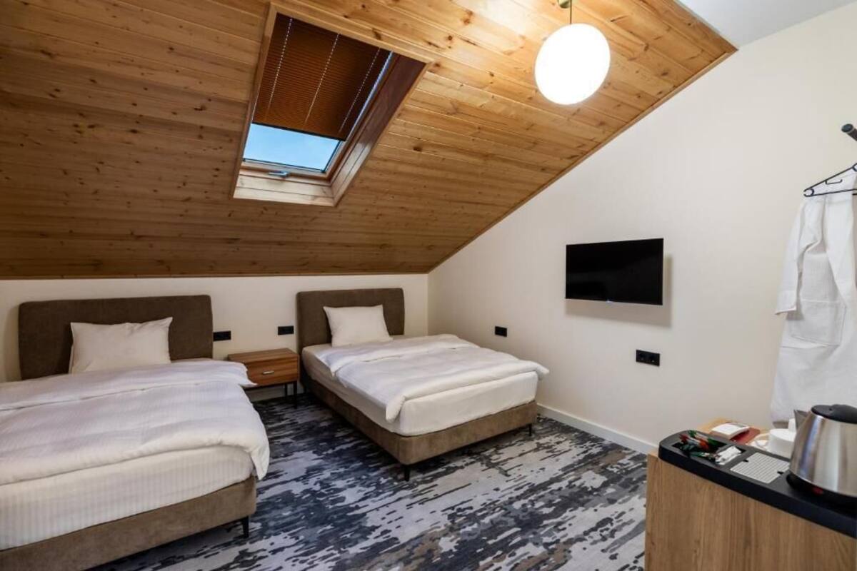 A room with two beds, a TV, a wooden ceiling, and a skylight.
