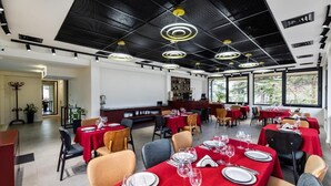 Un restaurante con mesas dispuestas para comer, una zona de bar y amplios ventanales que dejan entrar luz natural.