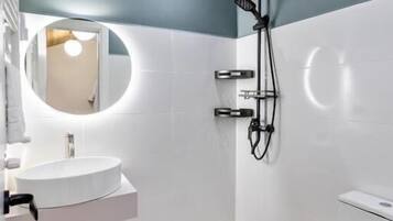 Un bagno moderno con un lavandino bianco, uno specchio rotondo, una doccia con un tubo nero e un water bianco.