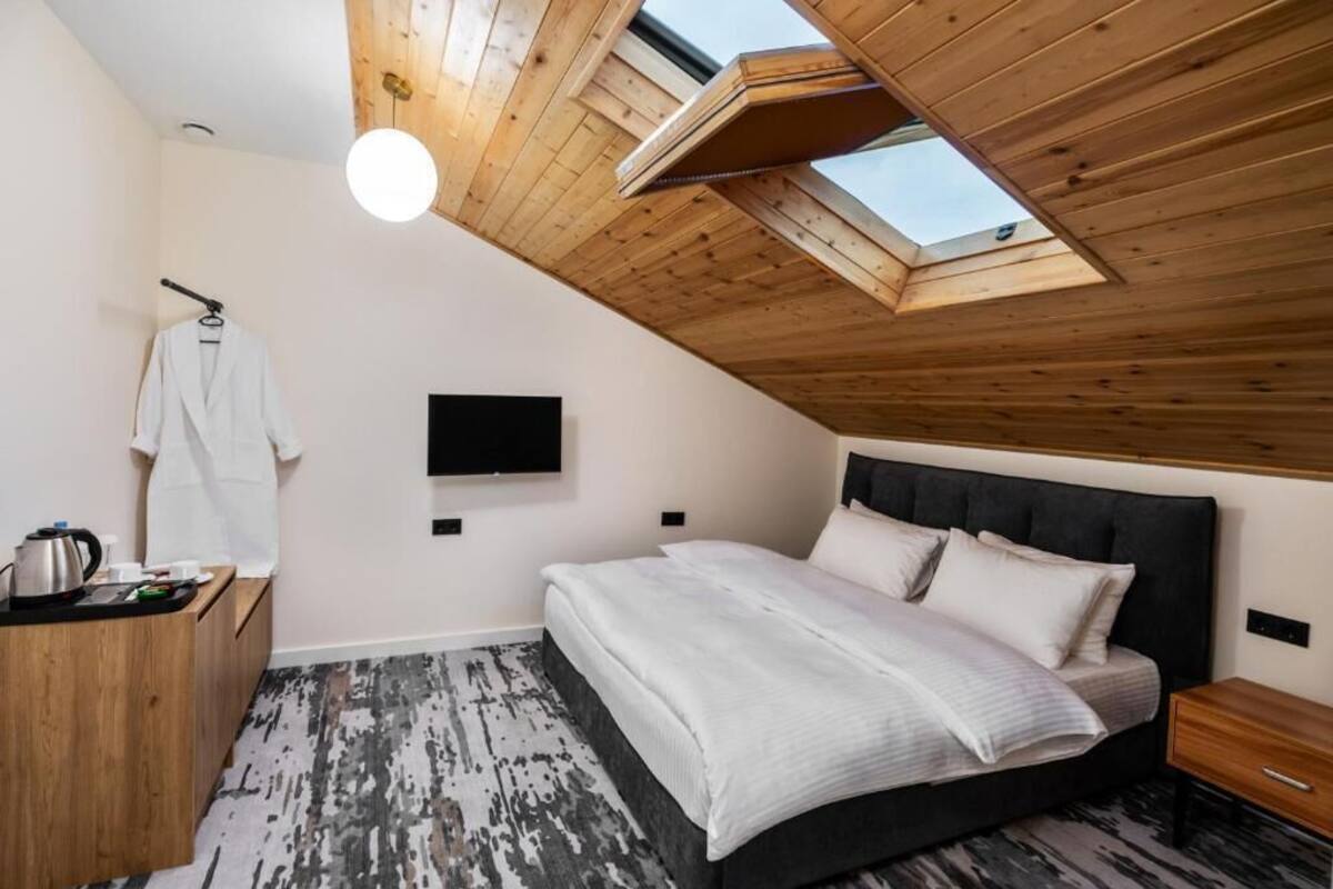 A bedroom with a sloped ceiling, a bed, a TV, a wooden dresser, and a skylight.