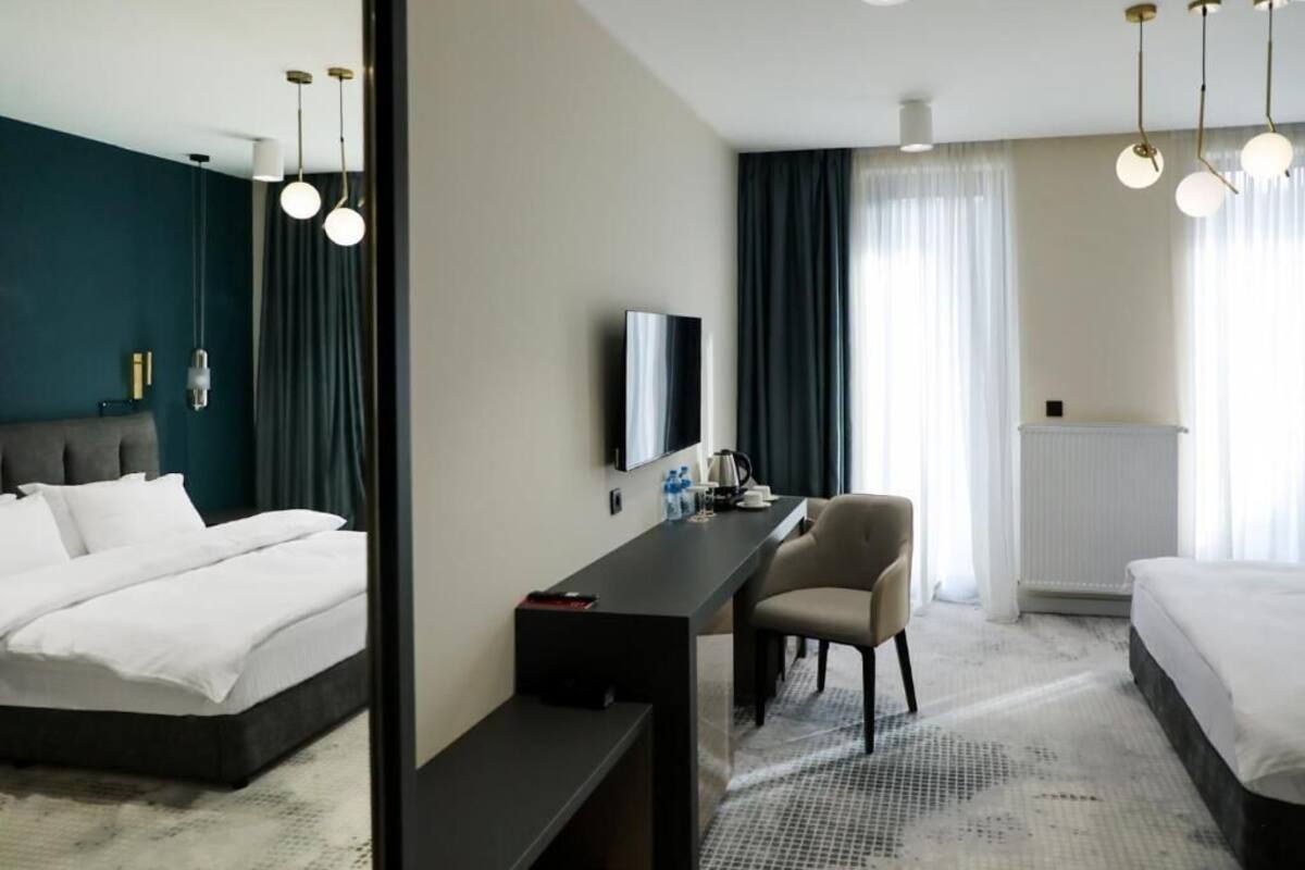 A hotel room with a bed, a desk, a chair, a TV, and a window with curtains.