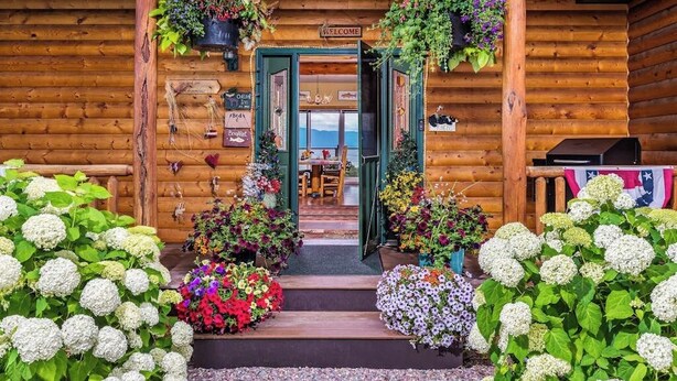 Eine Holzhütte mit einladendem Eingang, einem 'WELCOME'-Schild und Blick ins Innere.