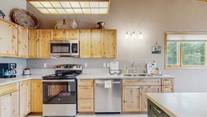 Una cocina con armarios de madera, electrodomésticos de acero inoxidable, lavavajillas y una ventana con vistas a zonas verdes.
