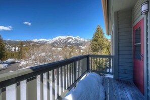 A wooden deck with a railing, a red door, and a view of snow-covered mountains. - Townhome minutes from slopes (Big Sky)