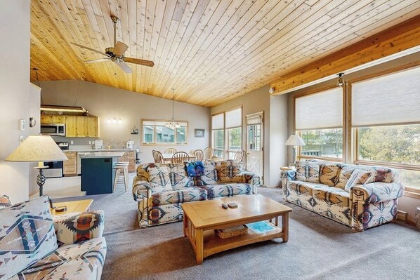 A spacious living area with a wooden ceiling, a sofa set, a coffee table, and a kitchen in the background. - Townhome minutes from slopes (Big Sky)