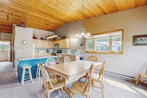 A kitchen with wooden cabinets, a central island with stools, a dining table with chairs, and a hanging light fixture. - Townhome minutes from slopes (Big Sky)