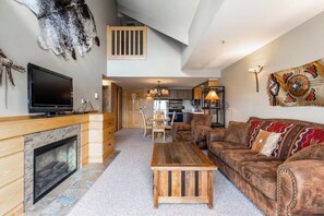 A spacious living room with a fireplace, leather sofa, and a television. - Slope side family fun condo with shared pool and hot tub (Big Sky)