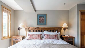 Un dormitorio con cabecera de madera, dos lámparas de noche, un cuadro enmarcado en la pared y una ventana a la izquierda.