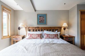 A bedroom with a wooden headboard, two bedside lamps, a framed picture on the wall, and a window on the left. - Slope side family fun condo with shared pool and hot tub (Big Sky)