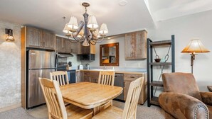 Una cocina moderna con armarios de madera, un refrigerador de acero inoxidable, una mesa de comedor con sillas y una lámpara de araña.
