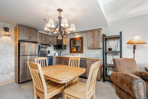 A modern kitchen with wooden cabinets, a stainless steel refrigerator, a dining table with chairs, and a chandelier. - Slope side family fun condo with shared pool and hot tub (Big Sky)
