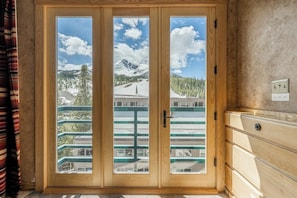Ein Zimmer mit einer Holztür, die auf einen Balkon mit Blick auf einen verschneiten Berg und ein Gebäude mit grüner Reling führt.