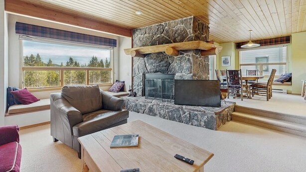 A cozy living room with a stone fireplace, leather sofa, and a coffee table. - Slopeside ski-in/ski-out condo with private hot tub & panoramic views (Big Sky)