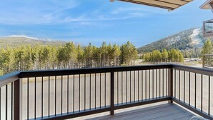 A wooden deck with a railing, overlooking a mountainous landscape with trees and a clear sky. - Slopeside ski-in/ski-out condo with private hot tub & panoramic views (Big Sky)