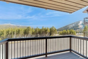 A wooden deck with a railing, overlooking a mountainous landscape with trees and a clear sky. - Slopeside ski-in/ski-out condo with private hot tub & panoramic views (Big Sky)