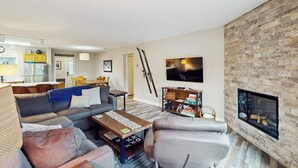 Una sala de estar con sofá, sillón, mesa de centro, chimenea, televisor y equipo de esquí.