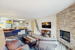 Ein Wohnzimmer mit Sofa, Sesseln, Couchtisch, Kamin, Fernseher und Skiausrüstung.