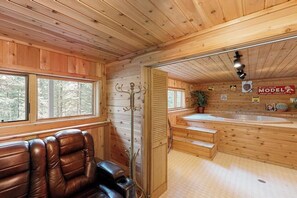 Ein Holzblockhaus-Interieur mit einer Sauna, einer Ledereinrichtung und Blick auf den Wald durch große Fenster.