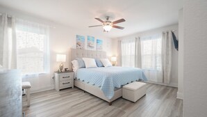 Ein Schlafzimmer mit Bett, Nachttischen, Deckenventilator und einem Fenster mit Vorhängen.