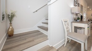 Eine Treppe mit Holzboden und einer weißen Wand, ein weißer Stuhl und ein kleiner Tisch mit einer Lampe.