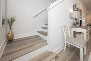 Eine Treppe mit Holzboden und einer weißen Wand, ein weißer Stuhl und ein kleiner Tisch mit einer Lampe.