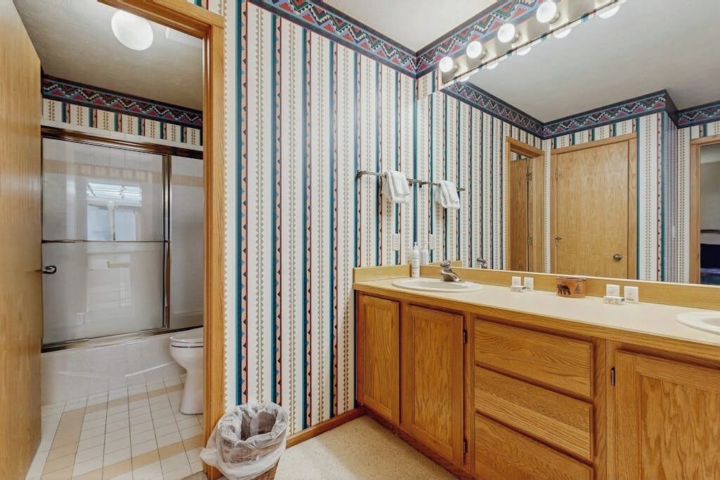 Een badkamer met gestreept behang, houten kastjes, een wastafel en een douche.