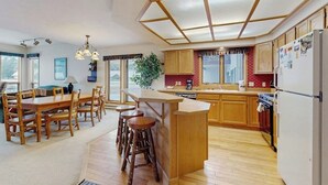 A kitchen with wooden cabinets, a central island with stools, a dining table with chairs, and a refrigerator. - Condo with WiFi, fireplace, hot tub, & swimming pool (Big Sky)