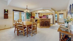 A spacious kitchen with wooden cabinets, a dining area with a wooden table and chairs, and a central island with stools. - Condo with WiFi, fireplace, hot tub, & swimming pool (Big Sky)