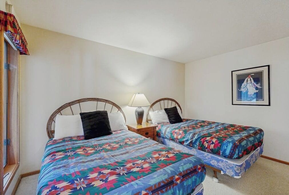 A room with two beds, a nightstand, a lamp, and a framed picture on the wall.