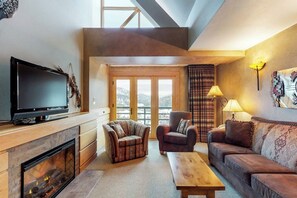 A living room with a fireplace, a television, and a sofa. - Condo with hot tub & pool - prime ski-in/out location (Big Sky)