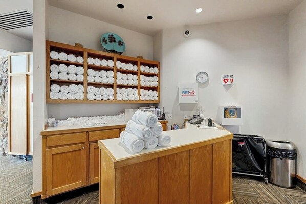 A hotel reception area with a wooden counter, a wall-mounted first-aid kit, and a trash bin.