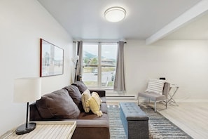 Ein modernes Wohnzimmer mit Sofa, Beistelltisch, Lampe, Bank und Blick ins Freie.