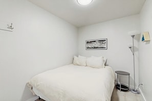 Ein Schlafzimmer mit einem Bett, einem Wandbild, einer Stehlampe und einem kleinen Tisch.