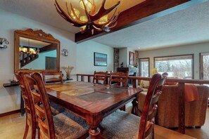 A dining area with a large wooden table, chairs, a chandelier, and a mirror on the wall. - Gorgeous country lodge with private sauna, deck & fireplace - near National Park (Jackson)