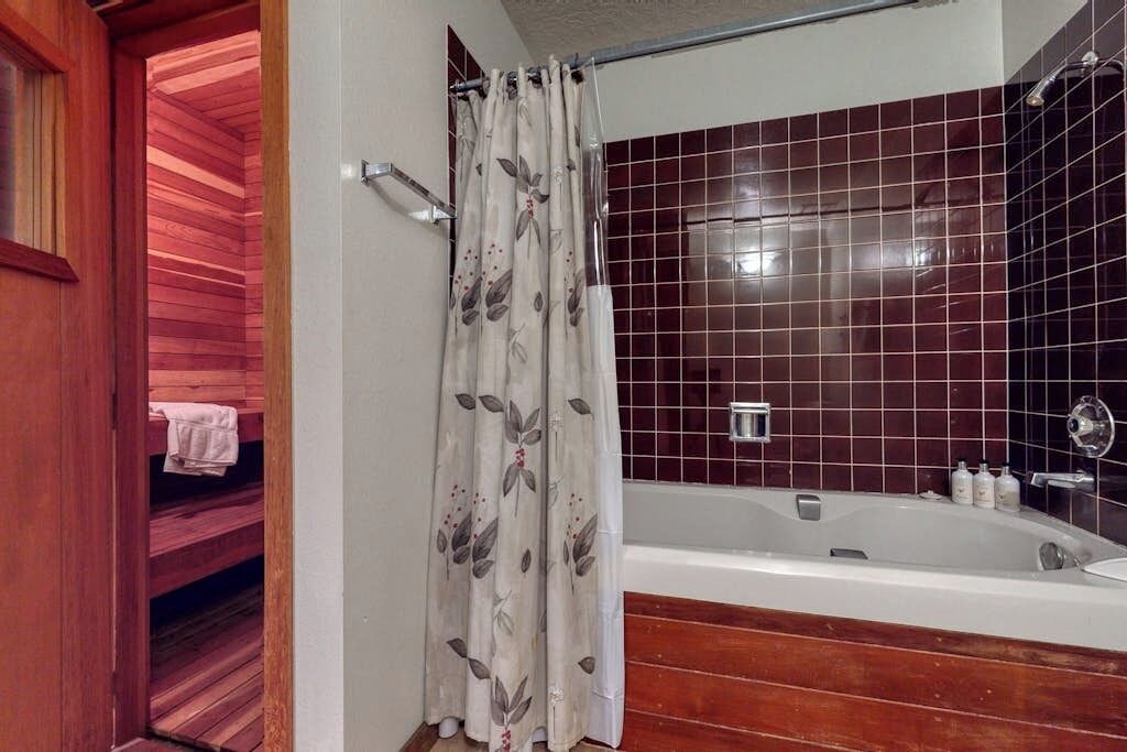 A bathroom with a bathtub, a shower curtain, and a wooden bench.