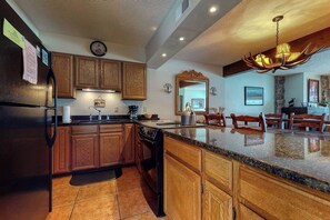 A kitchen with wooden cabinets, a granite countertop, a black refrigerator, and a unique antler chandelier. - Gorgeous country lodge with private sauna, deck & fireplace - near National Park (Jackson)