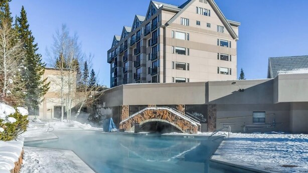 Un hotel moderno con piscina, arco de piedra y un edificio de varios pisos con balcones.