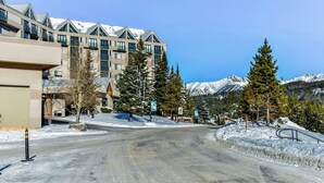 Una carretera cubierta de nieve que lleva a un edificio de diseño moderno, rodeado de montañas nevadas y árboles de hoja perenne.