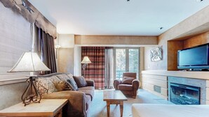 Habitación de hotel con sofá, sillón, mesa de centro, televisor, chimenea y ventanas amplias.