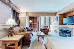 Ein Hotelzimmer mit einer Couch, einem Sessel, einem Couchtisch, einem Fernseher, einem Kamin und großen Fenstern.