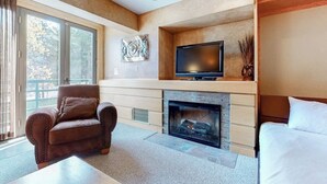 Una sala de estar moderna con chimenea, televisor, sofá y un ventanal grande.