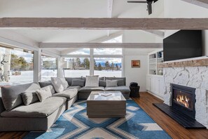 A modern living room with a sectional sofa, a fireplace, and large windows.