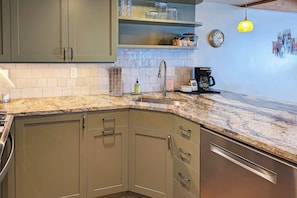 A kitchen with a granite countertop, stainless steel appliances, and a clock on the wall.
