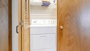 A laundry room with a white washer and dryer, wooden blinds, and a metal shelf with folded towels. - Gorgeous country escape with deck & wood-burning fireplace -  near hiking trails (Jackson)