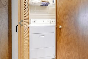 A laundry room with a white washer and dryer, wooden blinds, and a metal shelf with folded towels.