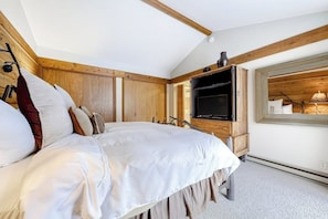 A bedroom with a bed, wooden walls, a television, and a window with a view.