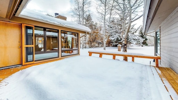A snow-covered deck with a wooden bench, a glass door leading to a room, and a snow-covered tree in the background. - Gorgeous country escape with deck & wood-burning fireplace -  near hiking trails (Jackson)