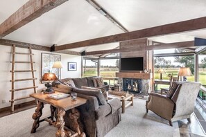 Ein geräumiges Wohnzimmer mit großem Fenster, Kamin und rustikalen Holzbalken.