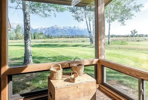 A room with large windows overlooking a grassy field and mountains. There are wooden baskets on a table in front of the windows. - Roomy townhome next to golf course with lovely deck & Teton views from living room (Jackson)
