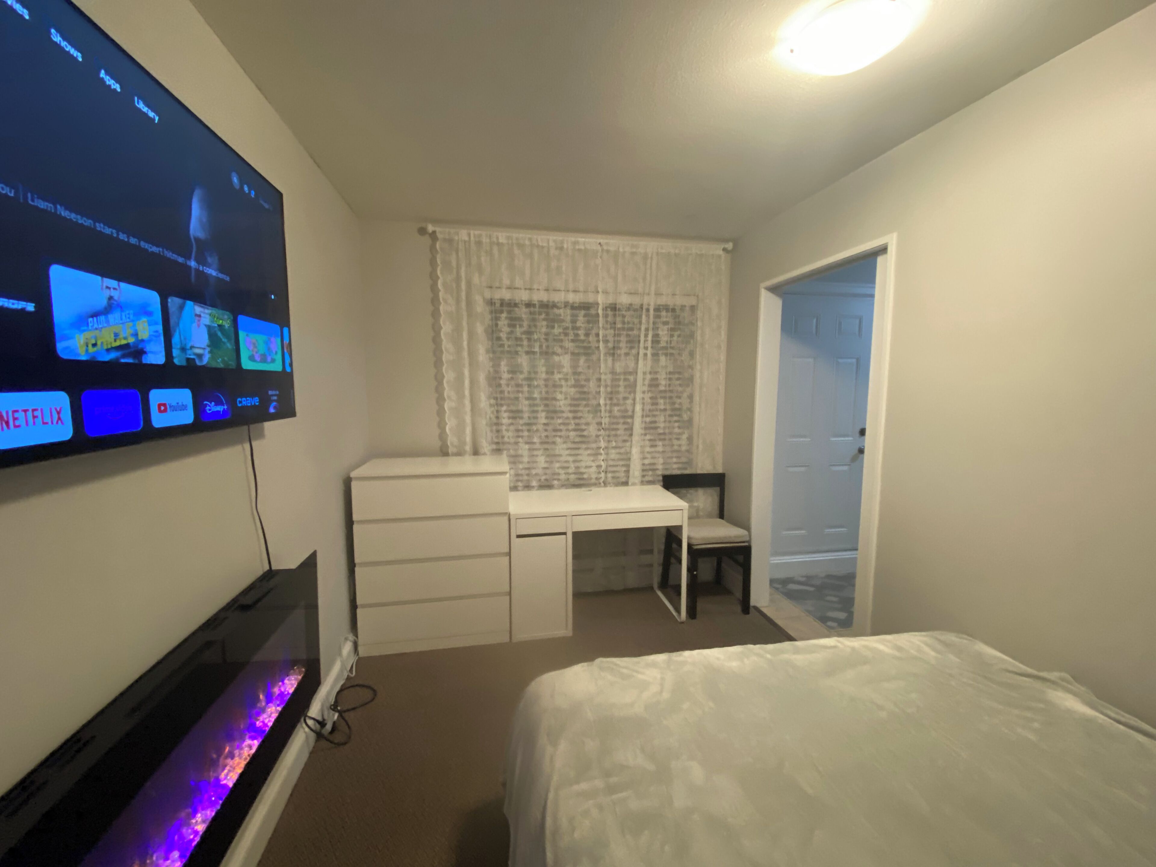 A bedroom with a bed, a desk, a chair, a TV mounted on the wall, and a door.